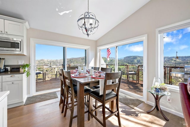 dining room featuring lofted ceiling, a chandelier, a mountain view, wood finished floors, and baseboards