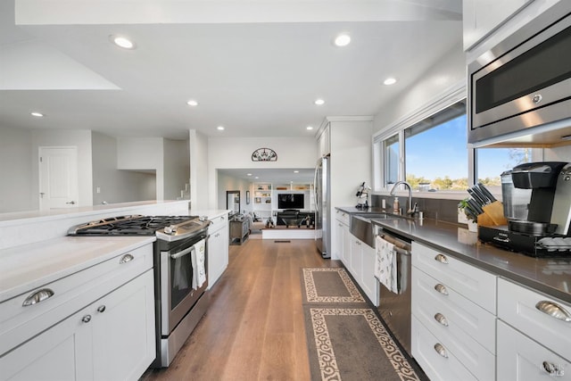 kitchen with wood finished floors, stainless steel appliances, white cabinetry, a sink, and recessed lighting