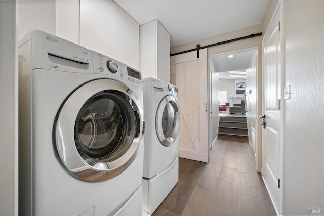 laundry area featuring wood finished floors, cabinet space, washing machine and clothes dryer, and a barn door