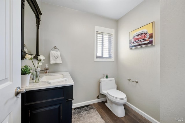 half bathroom featuring baseboards, vanity, toilet, and wood finished floors