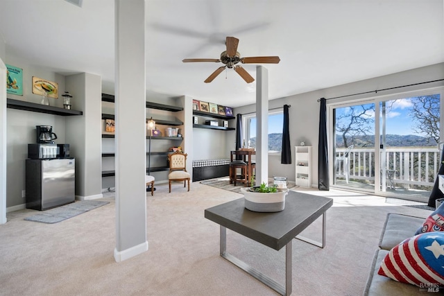 carpeted living room with built in shelves, baseboards, and a ceiling fan