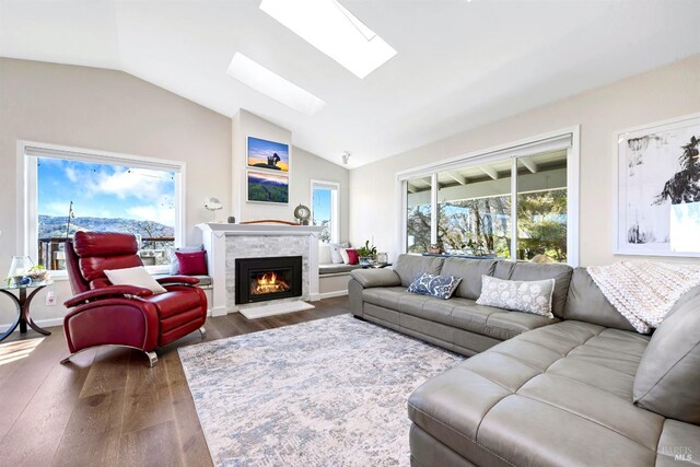 living area with vaulted ceiling with skylight, dark wood-style flooring, and a fireplace with flush hearth