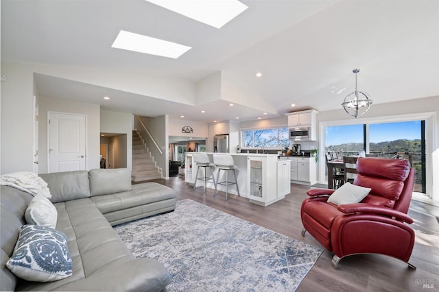 living area with vaulted ceiling with skylight, wood finished floors, recessed lighting, and an inviting chandelier