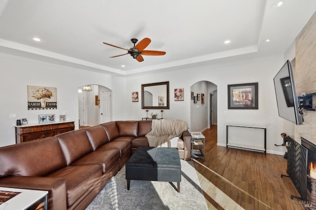 living area with arched walkways, a raised ceiling, and wood finished floors