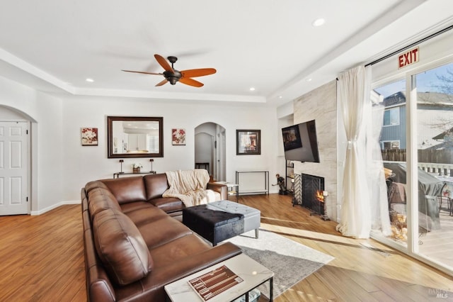 living room with a fireplace, arched walkways, a raised ceiling, and wood finished floors