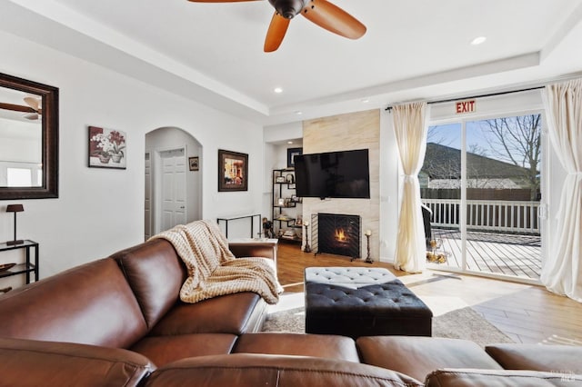 living room featuring arched walkways, recessed lighting, a premium fireplace, wood finished floors, and a tray ceiling