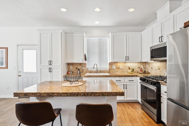 kitchen with light wood-style flooring, appliances with stainless steel finishes, a kitchen breakfast bar, white cabinetry, and a sink