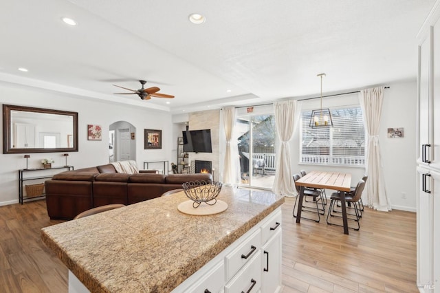 kitchen featuring arched walkways, a tray ceiling, light wood-style floors, a large fireplace, and white cabinets