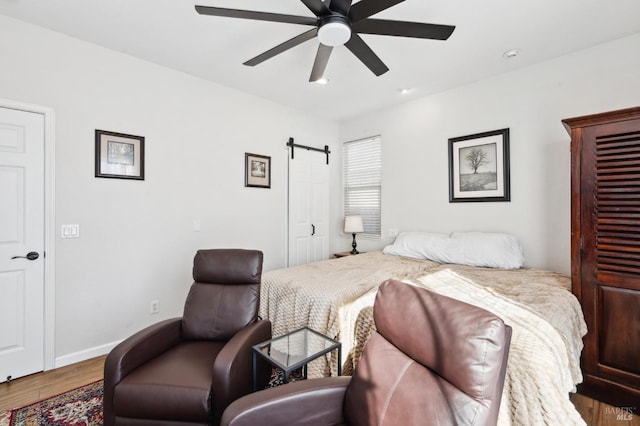 bedroom featuring a barn door, baseboards, ceiling fan, and wood finished floors