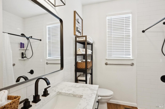 full bath with a tile shower, vanity, toilet, and wood finished floors