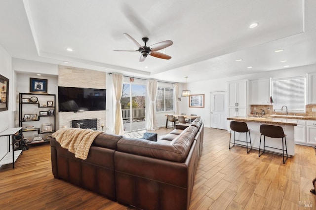 living area featuring light wood-style floors, a fireplace, a raised ceiling, and recessed lighting