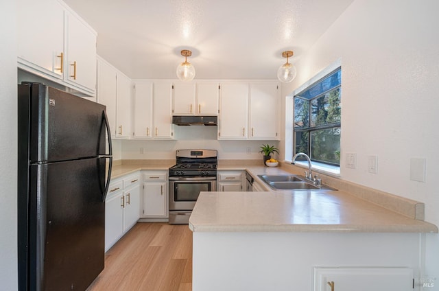 kitchen with under cabinet range hood, a peninsula, a sink, stainless steel range with gas cooktop, and freestanding refrigerator