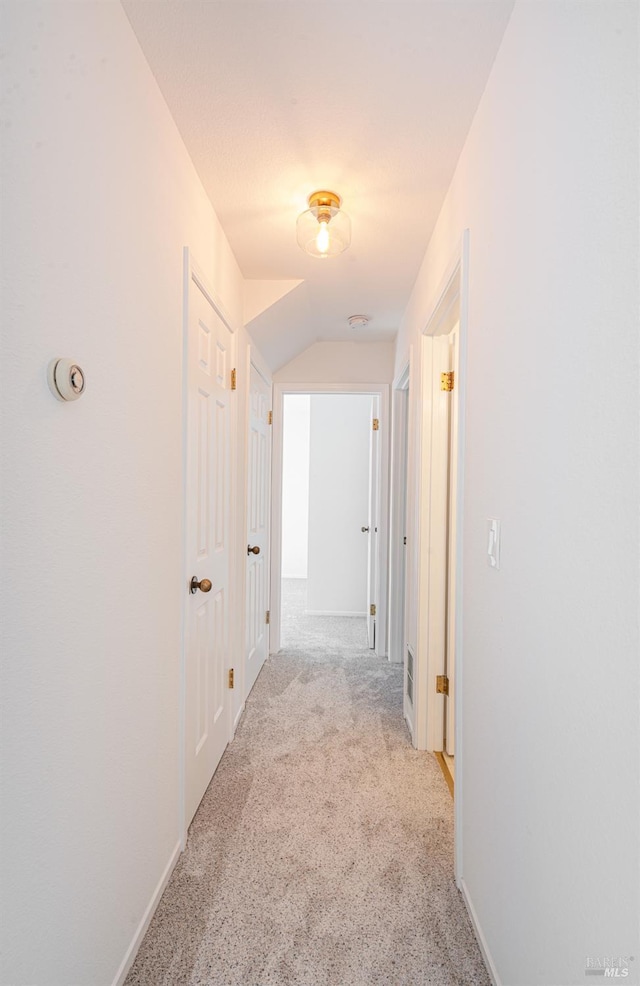 hall featuring lofted ceiling, carpet flooring, and baseboards