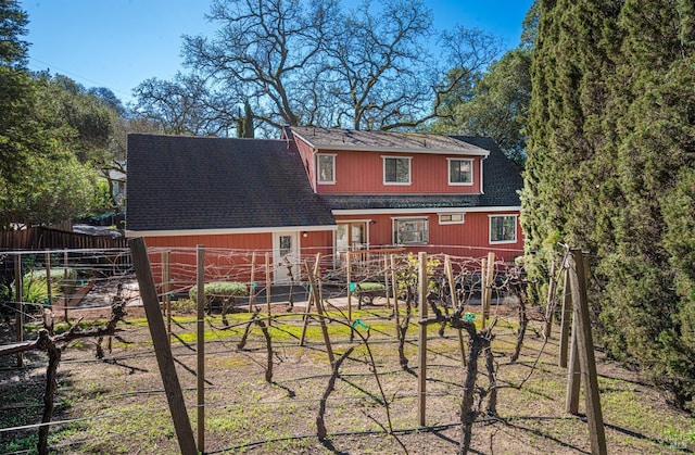 rear view of property featuring a shingled roof and fence