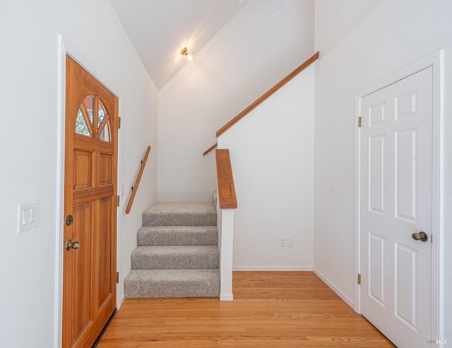 foyer entrance featuring stairs, light wood finished floors, lofted ceiling, and baseboards