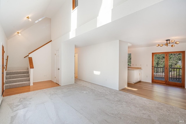 unfurnished living room with high vaulted ceiling, stairway, carpet, and wood finished floors