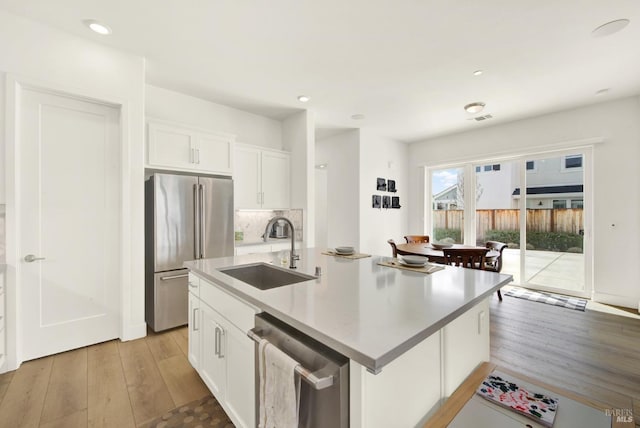 kitchen with a sink, white cabinetry, light wood-style floors, appliances with stainless steel finishes, and light countertops