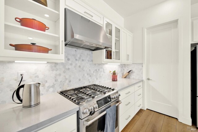 kitchen featuring wall chimney range hood, decorative backsplash, light wood-style floors, white cabinets, and gas stove