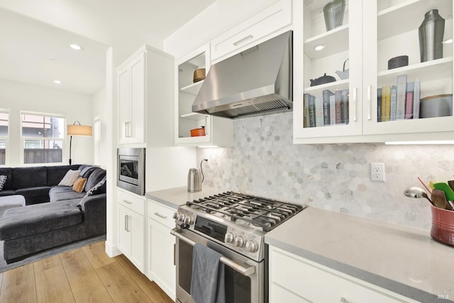 kitchen featuring stainless steel appliances, light countertops, light wood-style floors, wall chimney exhaust hood, and open floor plan