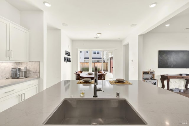 kitchen with light stone countertops, recessed lighting, a sink, white cabinetry, and backsplash