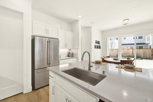 kitchen featuring high end refrigerator, white cabinets, light stone countertops, and a sink