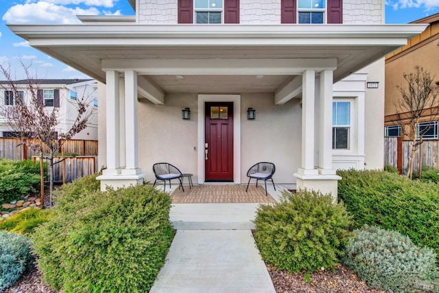 entrance to property featuring a porch, fence, and stucco siding