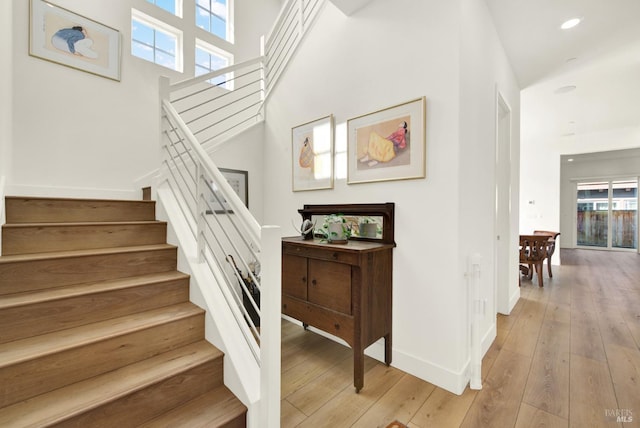 staircase with a high ceiling, recessed lighting, baseboards, and wood-type flooring