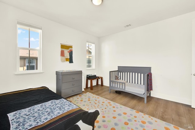 bedroom with hardwood / wood-style floors, multiple windows, and visible vents