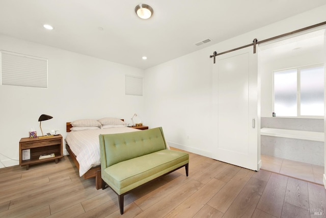 bedroom with a barn door, recessed lighting, light wood-style floors, and visible vents