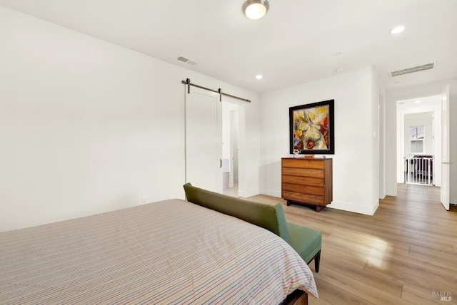 bedroom with recessed lighting, visible vents, a barn door, and light wood-style floors