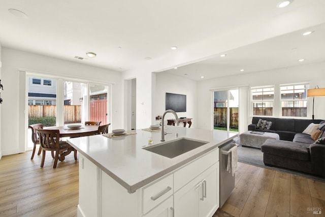 kitchen with light wood-style flooring, a sink, light countertops, stainless steel dishwasher, and open floor plan