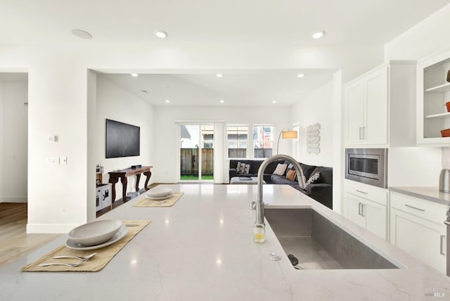 kitchen with light stone counters, a sink, white cabinetry, stainless steel microwave, and open floor plan