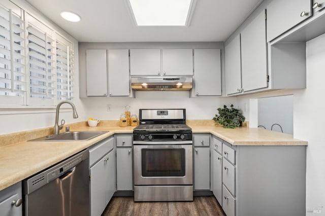 kitchen with dark wood-style flooring, stainless steel appliances, light countertops, a sink, and under cabinet range hood