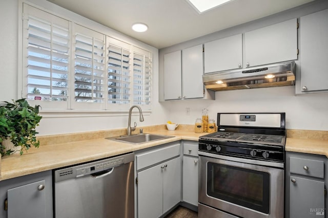 kitchen with appliances with stainless steel finishes, gray cabinets, light countertops, under cabinet range hood, and a sink