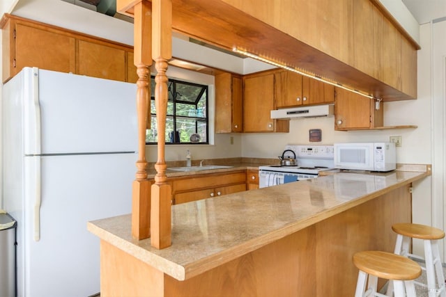 kitchen featuring brown cabinets, a sink, a peninsula, white appliances, and under cabinet range hood