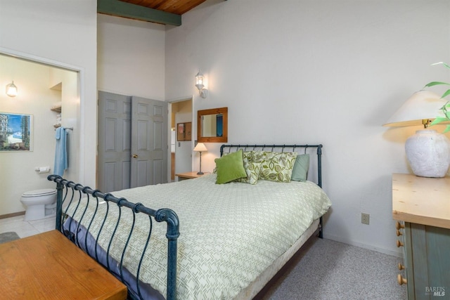 tiled bedroom featuring a high ceiling, beamed ceiling, ensuite bath, and baseboards