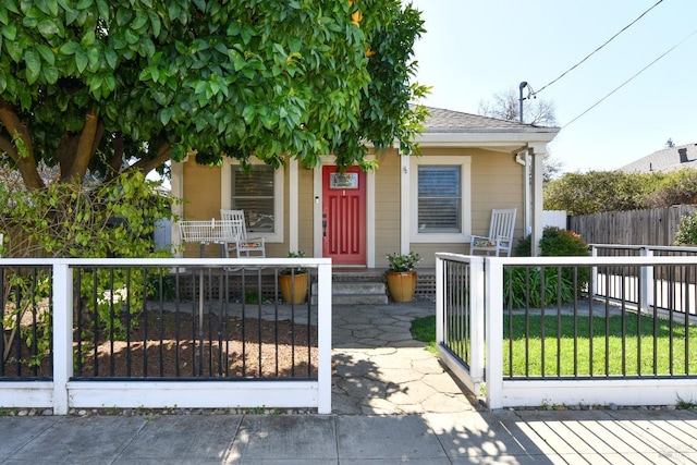 view of front of property with covered porch, a fenced front yard, a gate, and a shingled roof