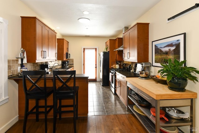 kitchen with tasteful backsplash, wall chimney exhaust hood, a kitchen breakfast bar, a peninsula, and stainless steel appliances