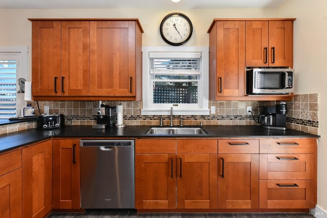 kitchen featuring stainless steel appliances, dark countertops, brown cabinets, and a sink