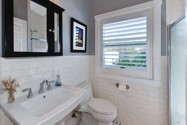 bathroom with toilet, tile walls, a sink, and a shower with shower door