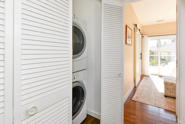 clothes washing area featuring dark wood-style floors, stacked washer and dryer, laundry area, and baseboards