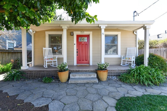 view of exterior entry featuring a porch and fence