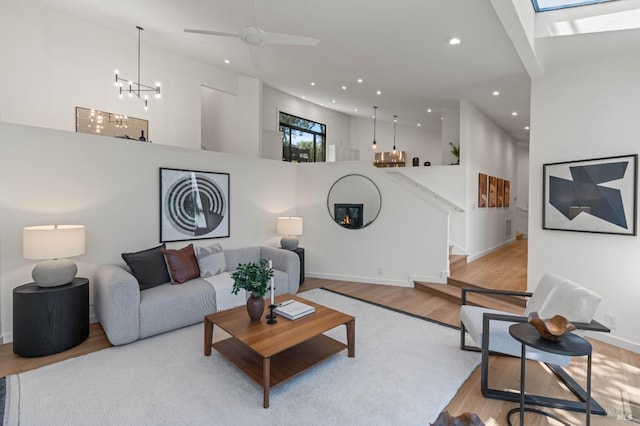 living area with recessed lighting, ceiling fan with notable chandelier, a high ceiling, wood finished floors, and stairs