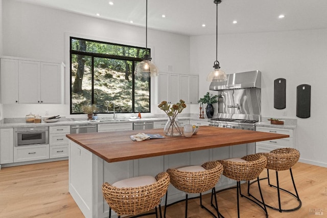 kitchen with a towering ceiling, light wood-style floors, white cabinetry, butcher block countertops, and wall chimney exhaust hood