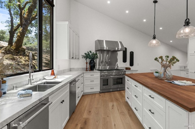 kitchen featuring butcher block counters, appliances with stainless steel finishes, light wood-type flooring, wall chimney range hood, and a sink