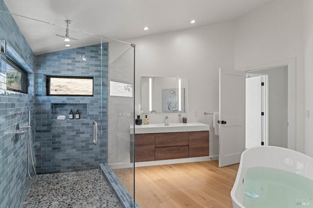 bathroom with lofted ceiling, wood finished floors, vanity, a freestanding bath, and a stall shower