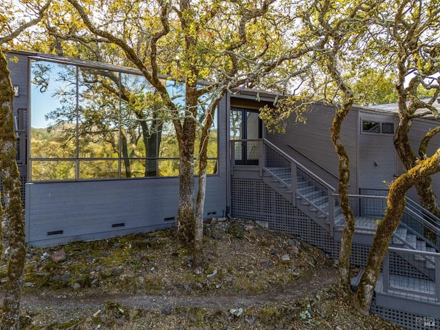 view of home's exterior with crawl space, a sunroom, and stairs