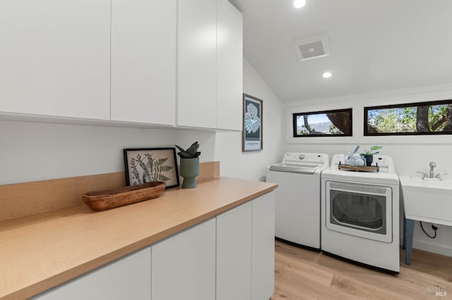 clothes washing area featuring light wood-style flooring, a sink, visible vents, cabinet space, and washer and clothes dryer