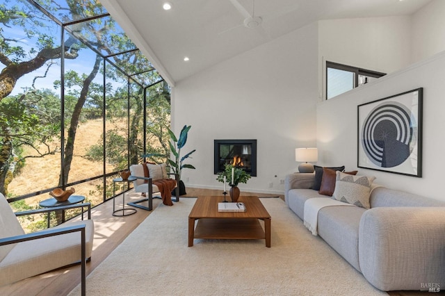 living room featuring baseboards, a glass covered fireplace, wood finished floors, high vaulted ceiling, and recessed lighting