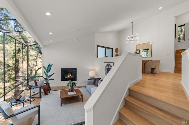 living area featuring a glass covered fireplace, wood finished floors, stairs, high vaulted ceiling, and recessed lighting